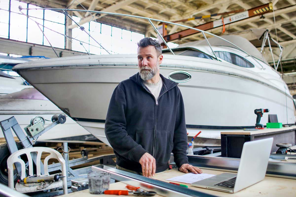 A person in a boat repair shop, surrounded by tools and a laptop, who uses the Coxswain 3 qualification for their duties