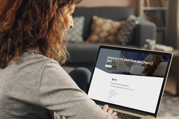 A person sitting on a couch using a laptop, with the screen displaying some online first aid training